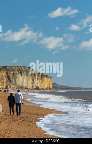 Giovane camminando lungo la spiaggia sotto il golden scogliere di arenaria a West Bay, bridport, Dorset, Inghilterra Foto Stock