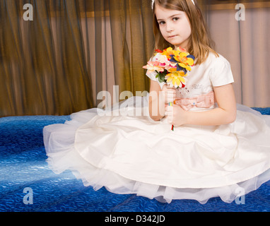 Bellissima bambina in posa seduta sul pavimento su una moquette blu in un tutu con la garza pellicolare gonna sparsi intorno a lei mentre lei tiene un bouquet di fiori nelle sue mani. Foto Stock