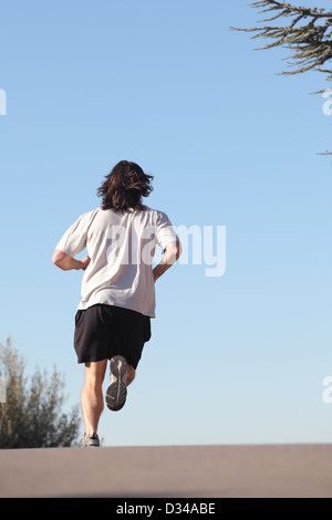 Vista posteriore di un uomo che corre su una strada con il cielo in background Foto Stock