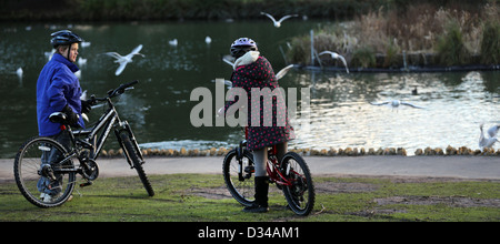 Bambini su moto guardando gli uccelli sul lago presso la Pittville Pump Room Pleasure Gardens Cheltenham Gloucestershire in Inghilterra Foto Stock