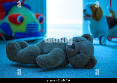 Brown orsacchiotto posa su un bambino il pavimento della camera. Le tonalità blu. Foto Stock