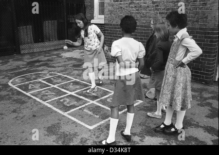 Bambini della scuola junior che giocano nel parco giochi Hopscotch. Londra sud. Inghilterra degli anni '70. Gruppo etnico misto di ragazze, BRAMONE nero britannico e bambini bianchi. 1975 REGNO UNITO HOMER SYKES Foto Stock