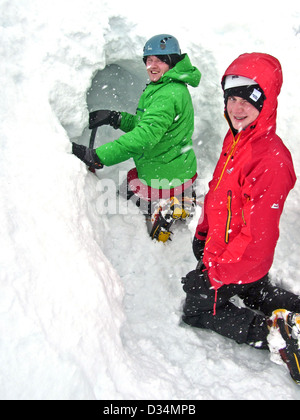 Due giovani uomini scavare un foro di neve nelle highlands scozzesi Foto Stock
