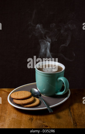 Una fumante tazza di una bevanda calda su un piattino con biscotti Foto Stock