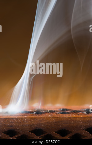 Brucia Incenso fumo vorticoso di deriva in una stanza buia da fori di uscita racchiusi in un supporto di legno Foto Stock