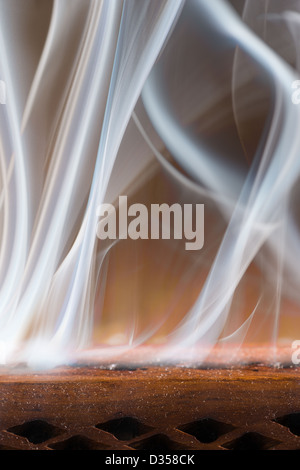 Brucia Incenso fumo vorticoso di deriva in una stanza buia da fori di uscita racchiusi in un supporto di legno Foto Stock