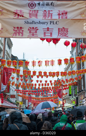 Segni lanterne e decorazioni con la folla sotto gli ombrelli Gerrard Street London REGNO UNITO al Capodanno cinese 2013 Foto Stock