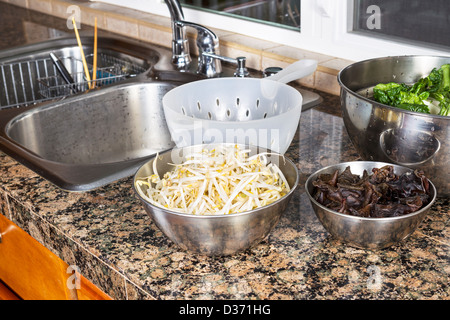 I germogli di soia, legno Cinesi le orecchie e Choy sulla parte superiore del banco di cucina accanto al lavello in acciaio inox con filtro a rete di plastica Foto Stock