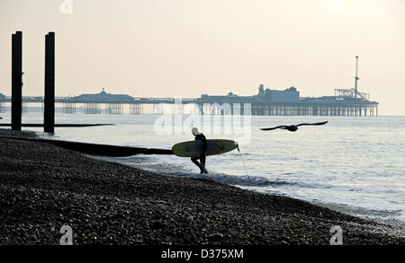 Brighton SUSSEX REGNO UNITO. 12 Febbraio 2013 - Surfer porta il suo bordo Fino la spiaggia di Brighton la mattina presto in inverno Foto Stock