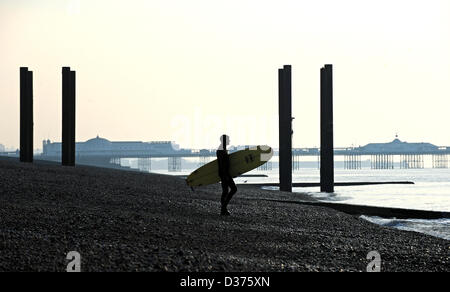 Brighton SUSSEX REGNO UNITO. 12 Febbraio 2013 - Surfer porta il suo bordo Fino la spiaggia di Brighton la mattina presto in inverno Foto Stock