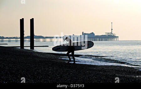 Brighton SUSSEX REGNO UNITO. 12 Febbraio 2013 - Surfer porta il suo bordo Fino la spiaggia di Brighton la mattina presto in inverno Foto Stock