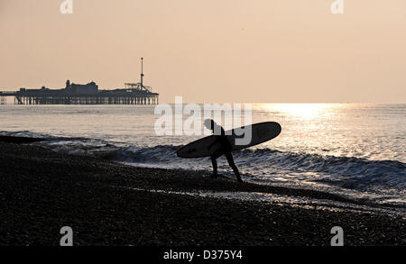 Brighton SUSSEX REGNO UNITO. 12 Febbraio 2013 - Surfer porta il suo bordo Fino la spiaggia di Brighton la mattina presto in inverno Foto Stock