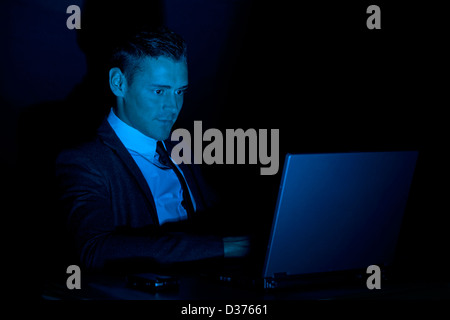 Uomo al lavoro su un computer portatile al buio, eventualmente attività illegali Foto Stock