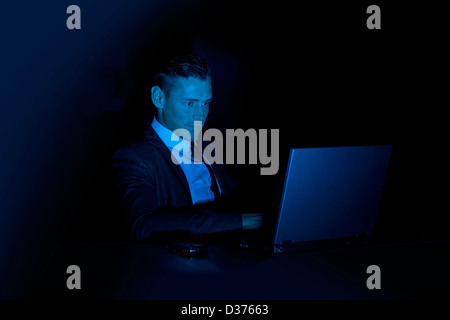 Uomo che lavora a un computer portatile in una stanza buia Foto Stock