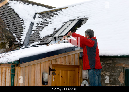 Un uomo si cancella per tutta la notte di neve da una tettoia in rural Aberdeenshire in Scozia. Foto Stock