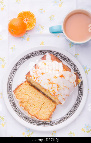 Citrus lemon orange clementina pioggerella ghiacciata di pan di spagna in casa su una tovaglia floreale con un Clementina e una tazza di tè. Foto Stock