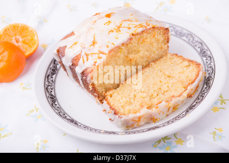 Citrus lemon orange clementina pioggerella ghiacciata di pan di spagna in casa su una tovaglia floreale con un Clementina. Foto Stock