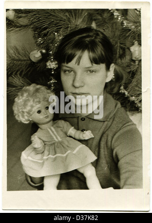 Vintage foto della ragazza giovane con bambola contro l'albero di Natale, circa 1969 Foto Stock