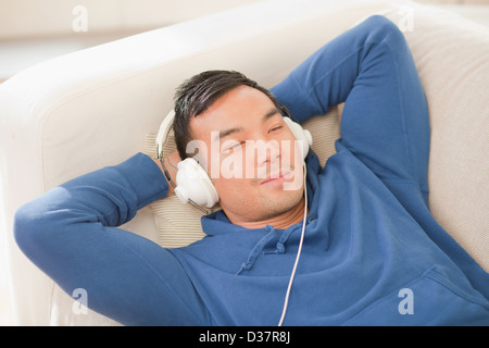 Uomo che ascolta le cuffie sul divano Foto Stock