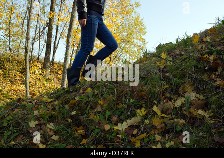 Ragazza in stivali di gomma salire a piedi sulla collina e Colore di autunno bella sunlighted alberi. Foto Stock