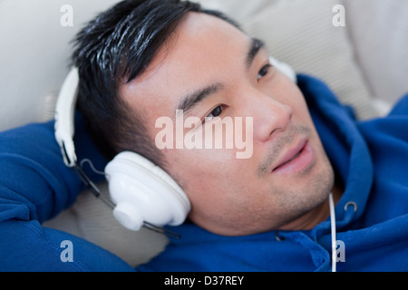 Uomo che ascolta le cuffie sul divano Foto Stock