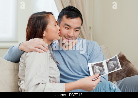 Giovane esaminando sonogram sul divano Foto Stock