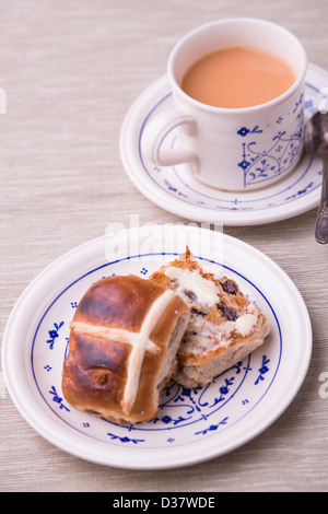 Tostare hot cross bun imburrato con una tazza di tè serviti su modellato cina vintage stoviglie su un tavolo neutro panno. Foto Stock