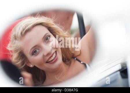 Donna sorridente riflessa in specchio auto Foto Stock