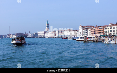 Un veneziano del taxi acqueo si fa strada lungo il Canale di San Marco sotto il sole con il Campanile di San Marco in background. Foto Stock