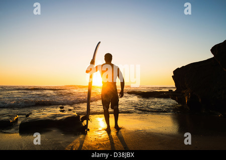 Uomo con la tavola da surf sulla spiaggia rocciosa Foto Stock