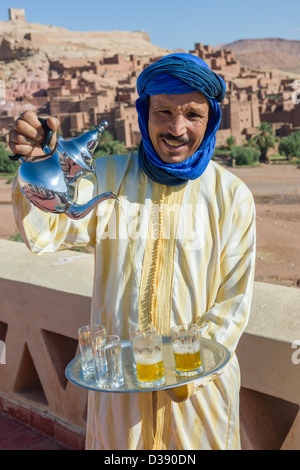 Hussein Boulkil, soprannominato " azione " versando il tè alla menta con il Ksar (borgo fortificato) dietro, Ait Benhaddou, Marocco Foto Stock