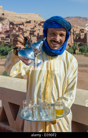 Hussein Boulkil, soprannominato " azione " versando il tè alla menta con il Ksar (borgo fortificato) dietro, Ait Benhaddou, Marocco Foto Stock