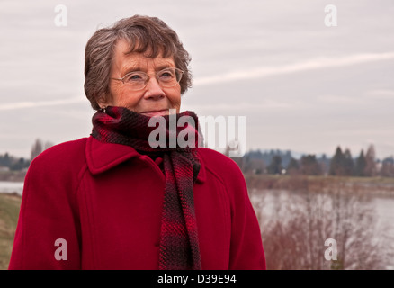 Ritratto di soggetti di razza caucasica senior citizen lady come essa si erge fuori al freddo. Sta indossando un rosso, rivestimento di lana e plaid sciarpa rossa Foto Stock