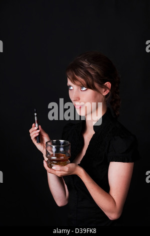 Piuttosto giovane donna con sigaretta elettrica e un bicchiere di whiskey e sfondo nero Foto Stock