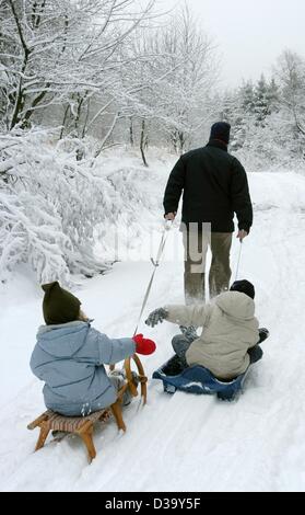 (Dpa) - Un padre le matasse i suoi due bambini su slittini attraverso il paesaggio innevato della Hoher Meissner Mountain, Germania, 23 dicembre 2003. Foto Stock