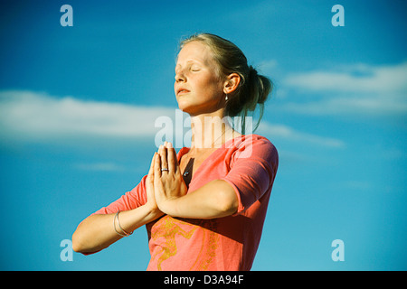 Donna meditando sotto il cielo blu Foto Stock