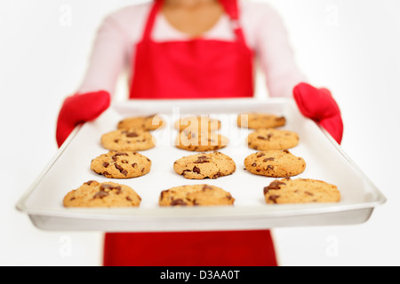 Giovani razza mista donna che mostra il vassoio con freschi di forno scaglie di cioccolato cookies isolati su sfondo bianco Foto Stock