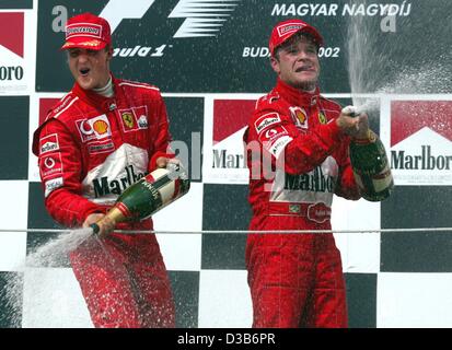 (Dpa) - Brasiliano pilota di Formula 1 Rubens Barrichello (R) e la sua Ferrari del team mate, il tedesco Michael Schumacher, allegria con una doccia di champagne sulla loro doppia vittoria dopo il Gran Premio di Ungheria sul circuito di Hungaroring vicino a Budapest, Ungheria, 18 agosto 2002. Barrichello ha vinto il primo posto e Schuma Foto Stock