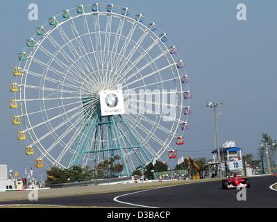 (Dpa) - tedesco di formula one champion Michael Schumacher gare passato una ruota panoramica di una vicina fiera del divertimento, durante i corsi di formazione di qualifica a Suzuka, in Giappone, 12 ottobre 2002. Foto Stock