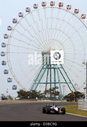 (Dpa) - Finlandese pilota di Formula Uno Kimi Raeikkoenen gare passato una ruota panoramica di una vicina fiera del divertimento, durante un corso di formazione a Suzuka, in Giappone, 11 ottobre 2002. Foto Stock