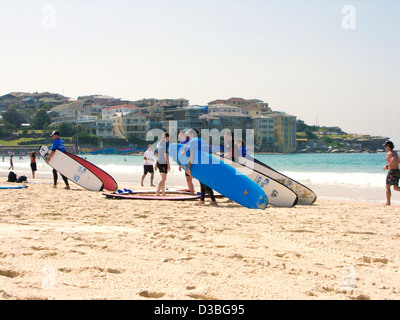 Persone che trasportano tavole da surf sulla spiaggia di bondi a Sydney, nuovo Galles del Sud, Australia e frequentano la scuola di surf Foto Stock