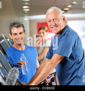 Felice l'uomo senior sul tapis roulant con un allenatore di fitness in palestra Foto Stock