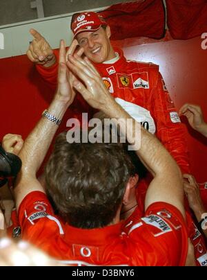 (Dpa) - Tedesco pilota di Formula Uno Michael Schumacher della Ferrari (fondo) è intriso di champagne come egli celebra i membri del team dopo la graffatura del campionato mondiale a seguito del giapponese di FORMULA ONE Grand Prix di Suzuka, 12 ottobre 2003. Schumacher posto 8th, conquistando un record sesto wor Foto Stock