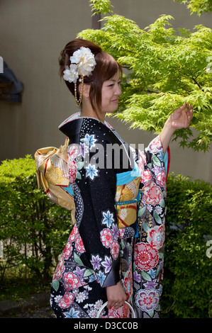 Carino, 20-qualcosa ragazza giapponese indossando il tradizionale furisode lungo il manicotto a kimono con molla design floreale pone a Fukui, Giappone Foto Stock