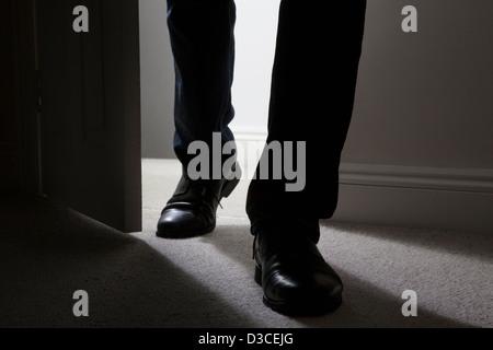 Close up di maschio adulto gambe e piedi indossando scarpe nere di entrare in una stanza buia. Silhouette. Foto Stock