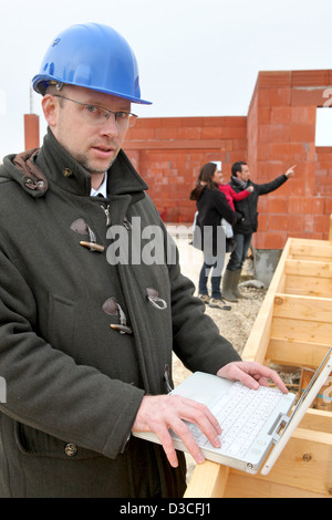 Helmeted architetto in cantiere utilizzando laptop Foto Stock