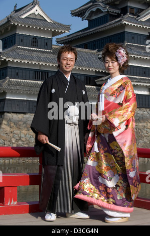 Sposi indossando il tradizionale kimono pongono di fronte a Matsumoto castello in una giornata di sole. Foto Stock