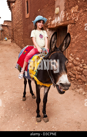 Ragazza asino di equitazione attraverso il tradizionale villaggio berbero, Marrakech, Marocco Foto Stock