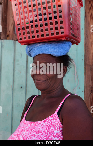 La donna da Vieux Fort Village, St Lucia portando i suoi messaggi in un rosso scatola di plastica e sulla sua testa Foto Stock