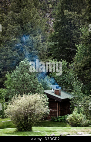 Fumo proveniente dal camino di log cabin sul cielo di montagna ranch, Montana, USA Foto Stock